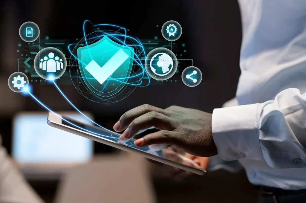 Close-up of a businessman's hands using a digital tablet with a glowing holographic overlay showing a checkmark shield, gear, and global network icons.
